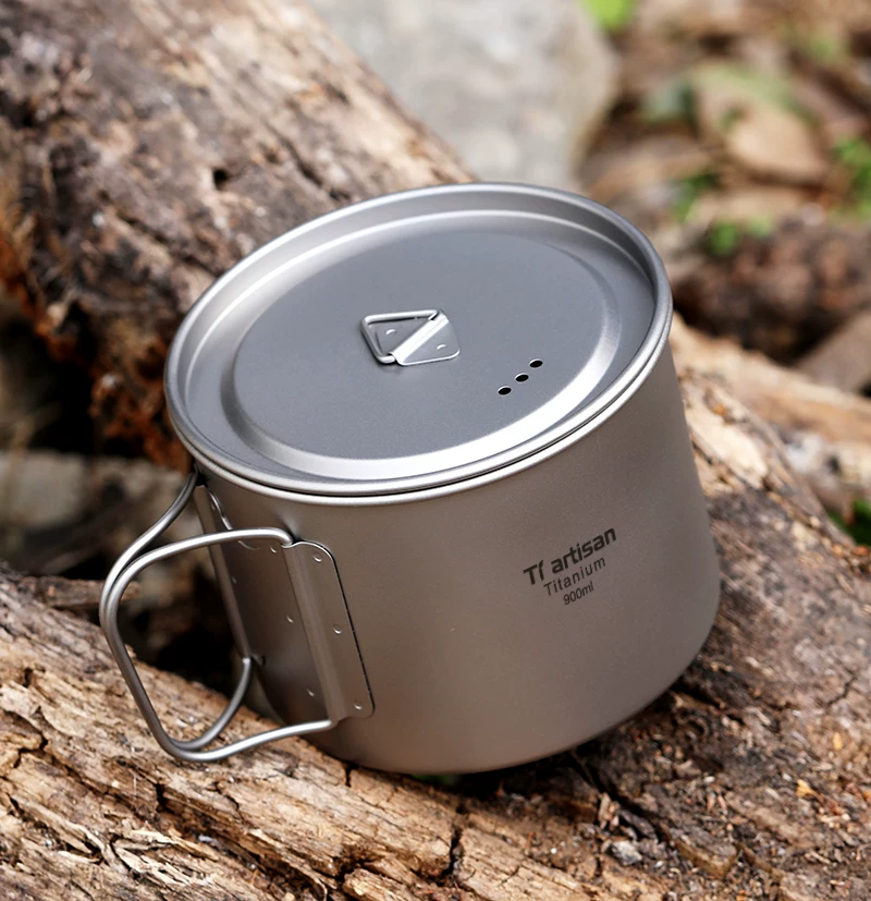 A titanium camping pot with lid resting on a log outdoors
